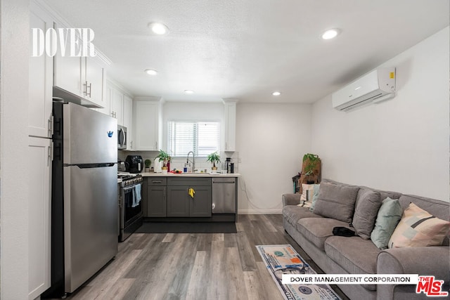 interior space featuring white cabinets, a wall mounted air conditioner, gray cabinetry, stainless steel appliances, and hardwood / wood-style floors