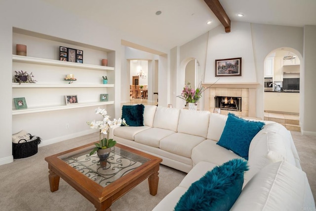 living room featuring lofted ceiling with beams, a tiled fireplace, light carpet, and built in shelves