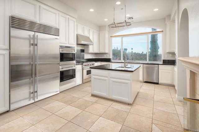 kitchen featuring decorative light fixtures, white cabinetry, light tile patterned floors, premium appliances, and a kitchen island with sink