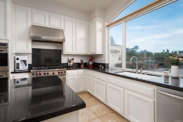 kitchen featuring appliances with stainless steel finishes, dark stone counters, sink, white cabinetry, and light tile patterned flooring