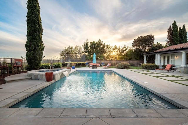 pool at dusk featuring pool water feature, a patio area, and an in ground hot tub