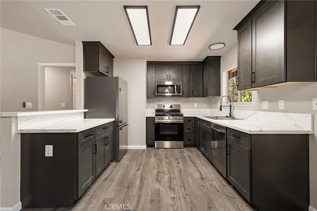 kitchen featuring light stone countertops, sink, lofted ceiling, appliances with stainless steel finishes, and light wood-type flooring