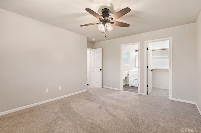 unfurnished bedroom featuring light carpet, ensuite bath, ceiling fan, a spacious closet, and a closet