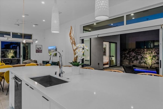 kitchen featuring pendant lighting, sink, stainless steel dishwasher, light tile patterned floors, and white cabinetry