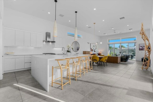 kitchen with white cabinets, wall chimney exhaust hood, pendant lighting, and a large island with sink