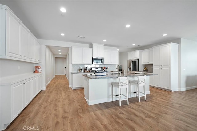 kitchen featuring white cabinetry, stainless steel appliances, and an island with sink