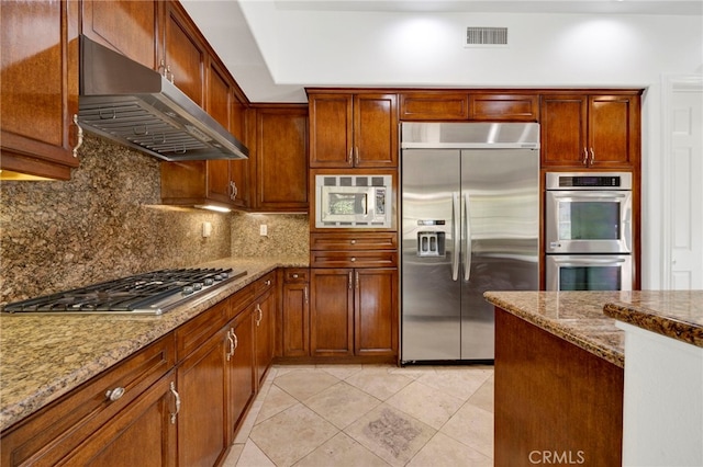 kitchen with light stone counters, light tile patterned flooring, built in appliances, and tasteful backsplash