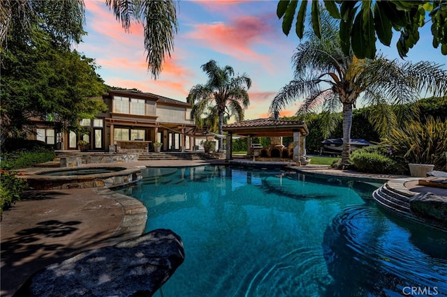 pool at dusk featuring a patio and an in ground hot tub