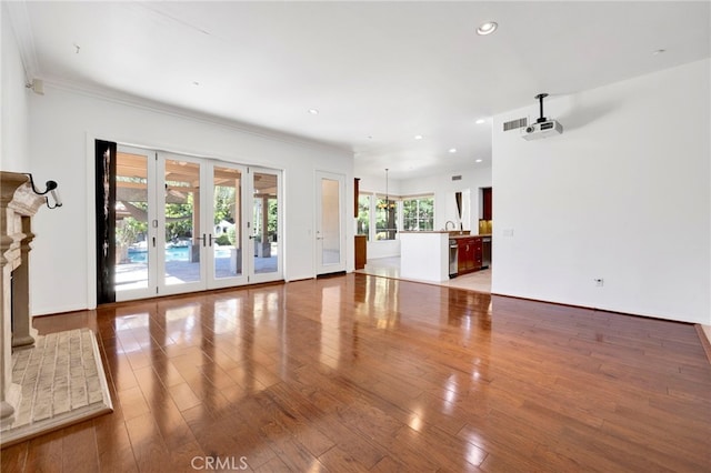 unfurnished living room featuring sink, hardwood / wood-style flooring, french doors, and crown molding