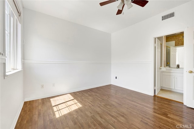 unfurnished bedroom with ensuite bath, dark wood-type flooring, and ceiling fan