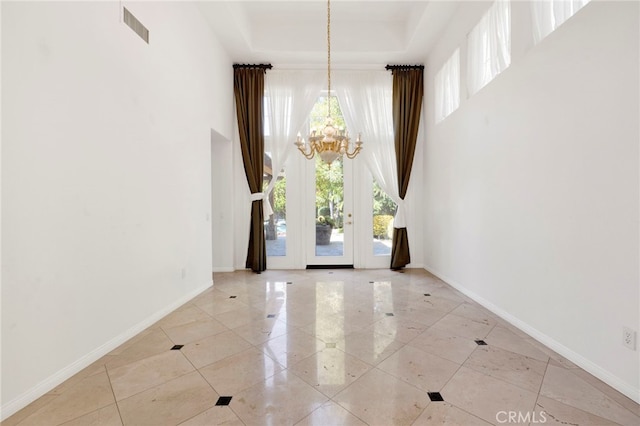 foyer entrance featuring a tray ceiling, french doors, and a notable chandelier