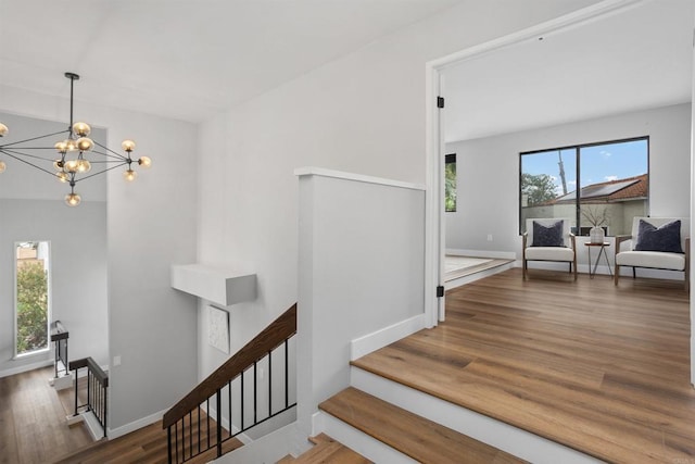 staircase with plenty of natural light, wood-type flooring, and an inviting chandelier