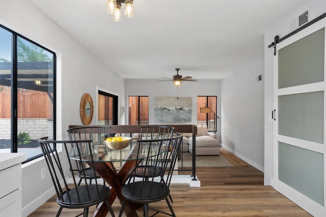 dining room with a barn door, ceiling fan, hardwood / wood-style floors, and a healthy amount of sunlight