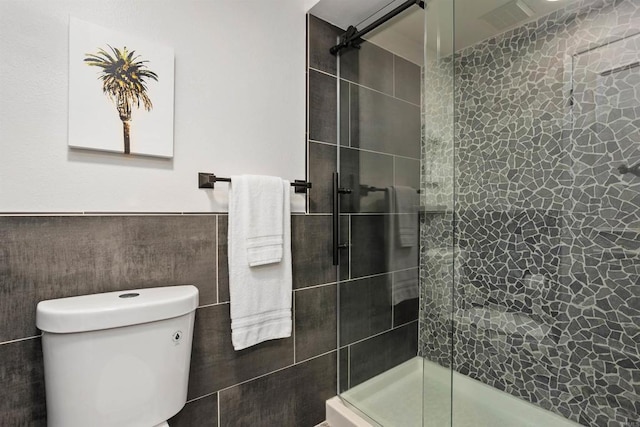 bathroom featuring toilet, a shower with door, and tile walls