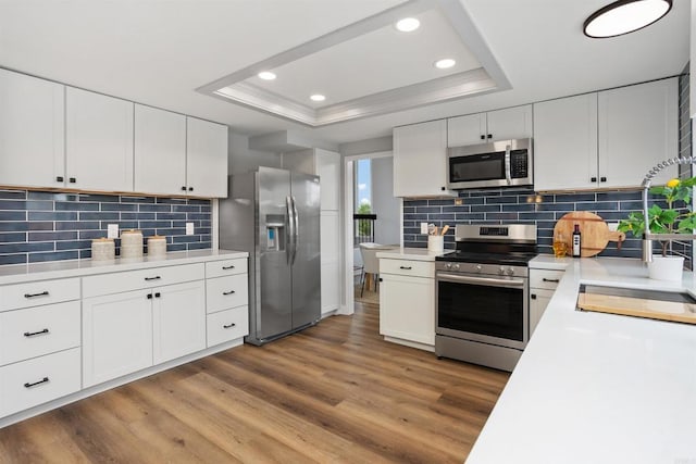 kitchen featuring appliances with stainless steel finishes, a tray ceiling, white cabinetry, and light hardwood / wood-style flooring