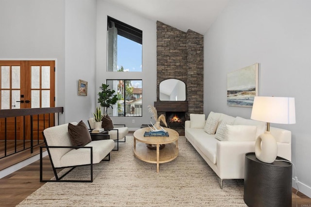 living room with a healthy amount of sunlight, a stone fireplace, wood-type flooring, and high vaulted ceiling