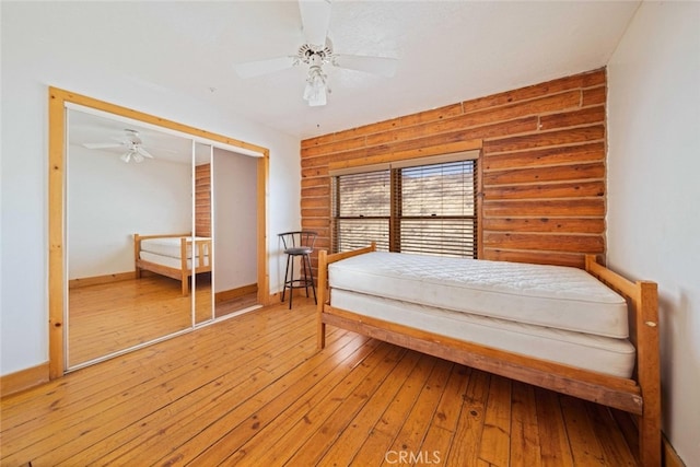 unfurnished bedroom with wooden walls, a closet, hardwood / wood-style flooring, and ceiling fan