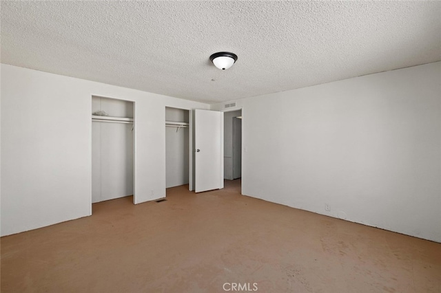 unfurnished bedroom with light carpet, two closets, and a textured ceiling