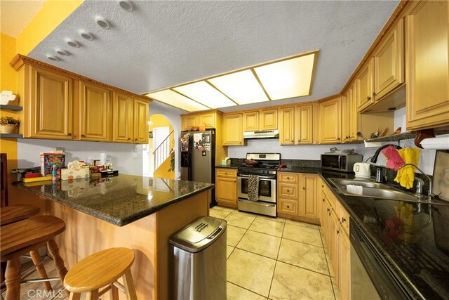 kitchen with a textured ceiling, kitchen peninsula, a kitchen breakfast bar, appliances with stainless steel finishes, and light tile patterned floors