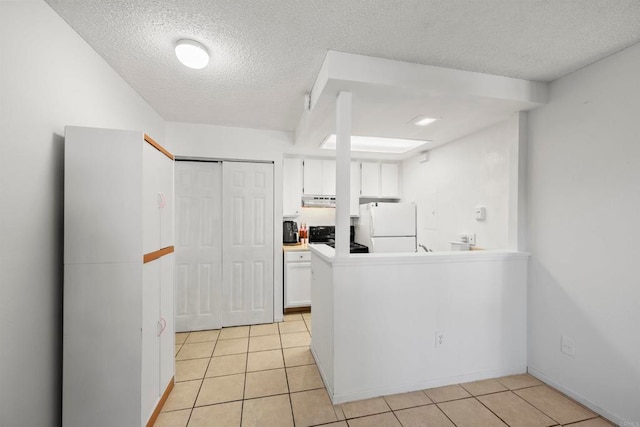 kitchen featuring white cabinets, white refrigerator, light tile patterned floors, and a textured ceiling