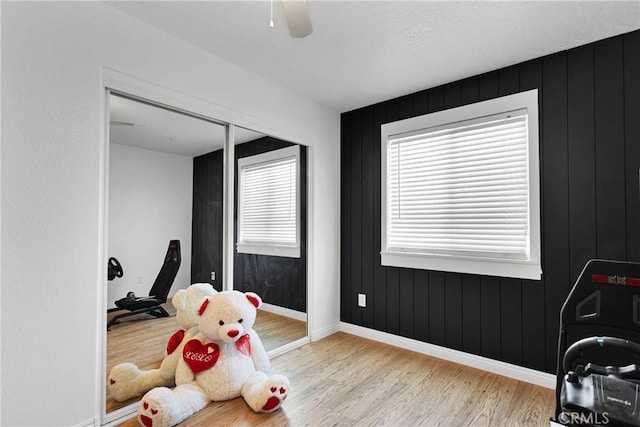 recreation room featuring wooden walls, ceiling fan, and light hardwood / wood-style floors