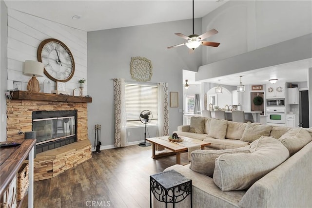 living room with high vaulted ceiling, ceiling fan, dark wood-type flooring, and a stone fireplace