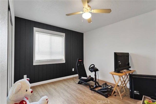 workout area with ceiling fan, wood walls, and light wood-type flooring