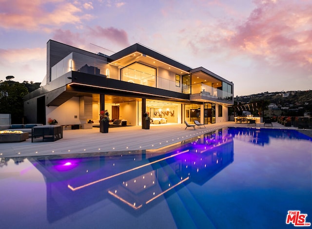 pool at dusk featuring an outdoor hangout area, a patio area, and a jacuzzi