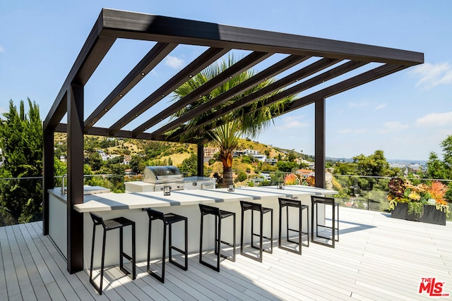 wooden terrace with a pergola, an outdoor kitchen, a bar, and grilling area