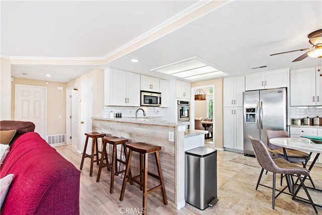 kitchen with kitchen peninsula, appliances with stainless steel finishes, backsplash, light stone counters, and white cabinetry