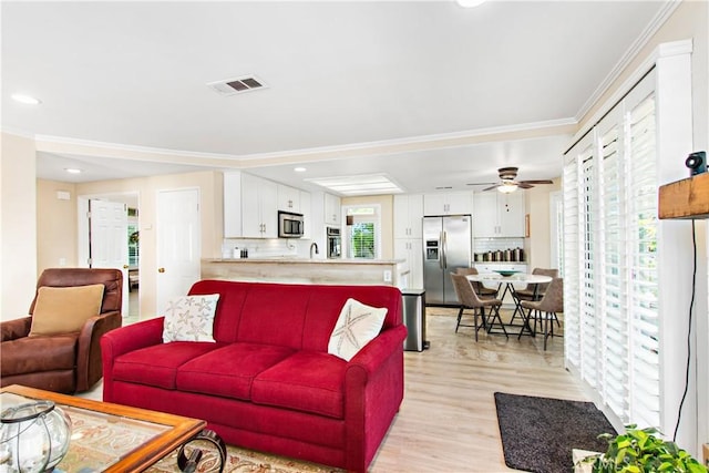 living room featuring ceiling fan, light hardwood / wood-style floors, ornamental molding, and a healthy amount of sunlight