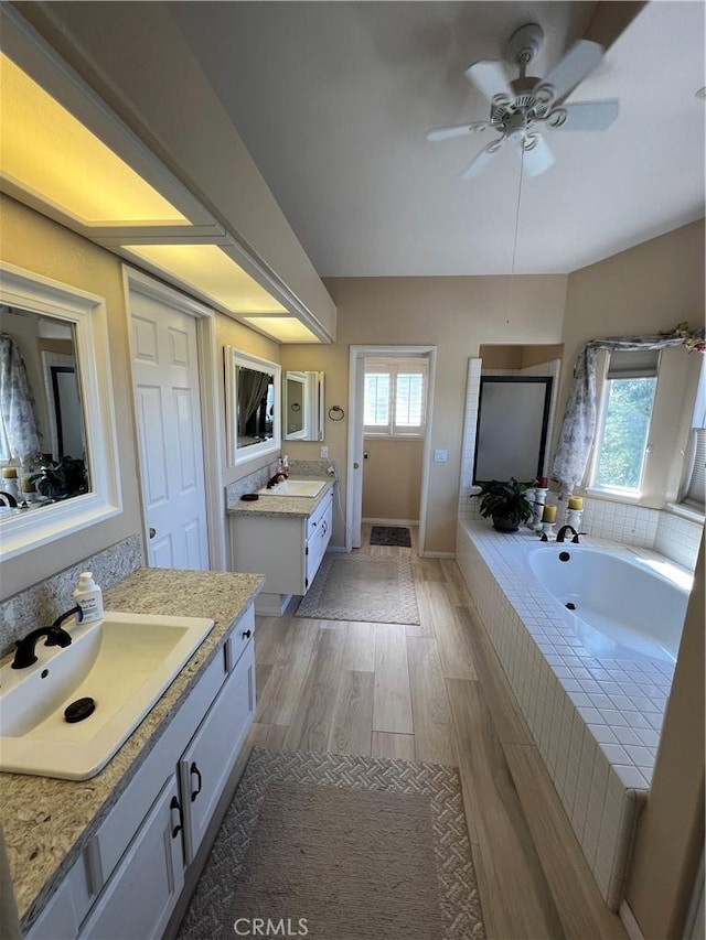 bathroom with vanity, ceiling fan, wood-type flooring, and tiled tub