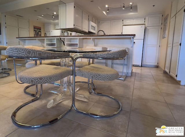 kitchen featuring light tile patterned floors, a kitchen bar, a tray ceiling, white appliances, and white cabinets