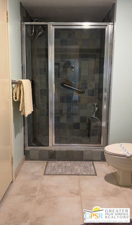 bathroom with a shower with shower door, toilet, and tile patterned flooring