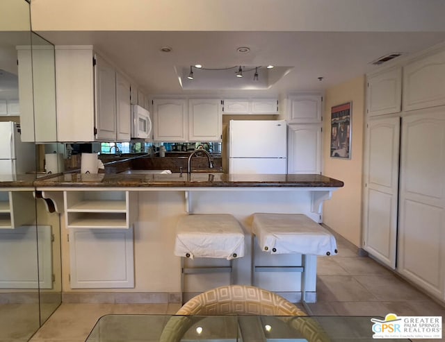 kitchen featuring white appliances, light tile patterned floors, white cabinets, kitchen peninsula, and a tray ceiling