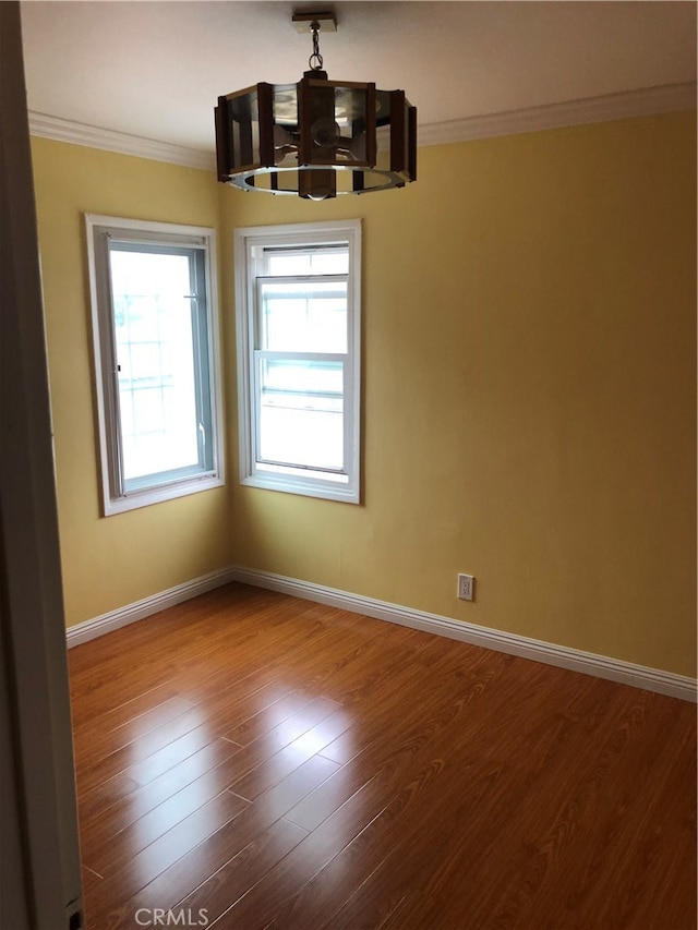 empty room featuring an inviting chandelier, ornamental molding, and hardwood / wood-style floors