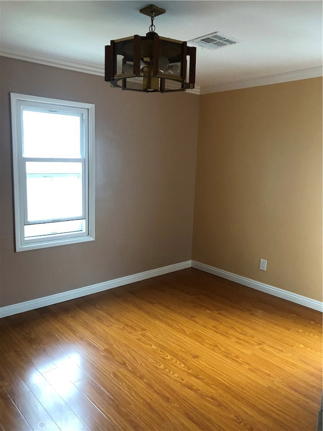 empty room with a chandelier, hardwood / wood-style floors, and crown molding