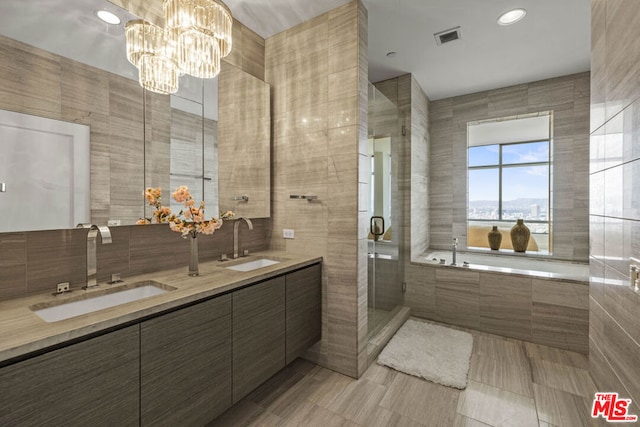 bathroom with an inviting chandelier, shower with separate bathtub, vanity, and tile walls