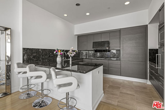 kitchen featuring a kitchen breakfast bar, decorative backsplash, kitchen peninsula, and dark stone countertops