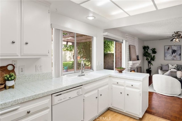 kitchen featuring dishwasher, kitchen peninsula, ceiling fan, a large fireplace, and white cabinetry