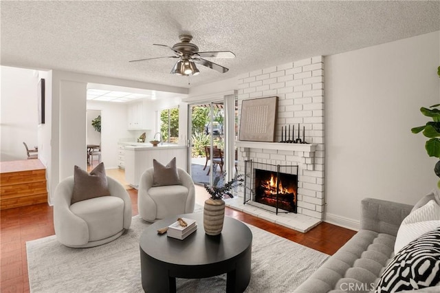 living room with a textured ceiling, hardwood / wood-style flooring, a brick fireplace, and ceiling fan