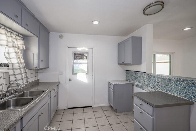 kitchen with light tile patterned floors, backsplash, gray cabinets, and sink