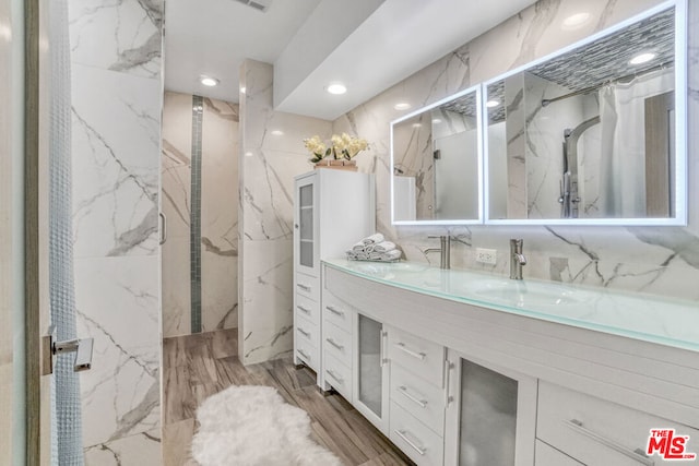 bathroom featuring hardwood / wood-style floors, vanity, a tile shower, and tile walls