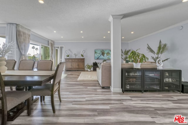 dining area featuring a textured ceiling, light hardwood / wood-style flooring, crown molding, and ornate columns