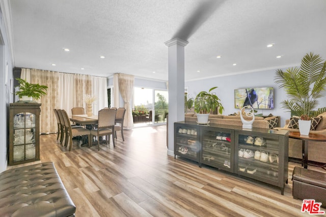 dining space featuring decorative columns, light hardwood / wood-style flooring, a textured ceiling, and ornamental molding