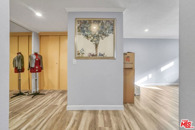 corridor featuring a textured ceiling, light hardwood / wood-style floors, and crown molding