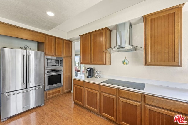 kitchen with wall chimney exhaust hood, a textured ceiling, appliances with stainless steel finishes, and light hardwood / wood-style flooring