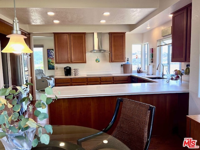 kitchen featuring kitchen peninsula, wall chimney exhaust hood, a textured ceiling, sink, and pendant lighting