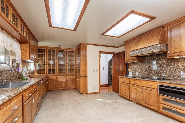 kitchen with decorative backsplash, premium range hood, ornamental molding, sink, and stone countertops