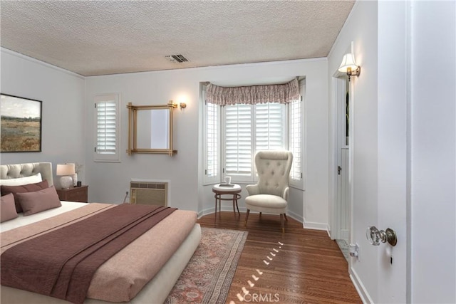 bedroom with a wall unit AC, dark wood-type flooring, and a textured ceiling